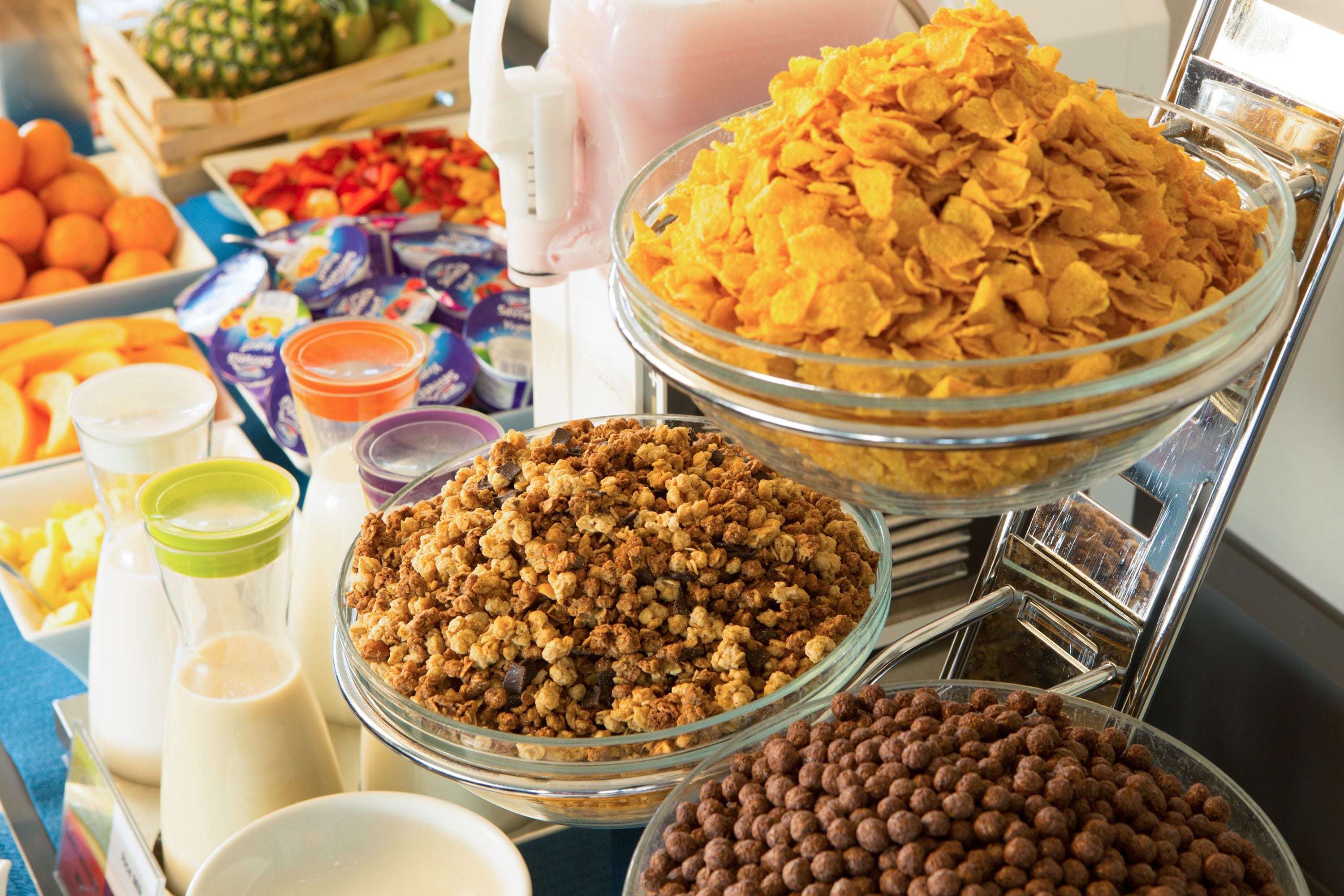 Buffet com diversas opções de alimentos, incluindo cereais, granola e bolinhas de chocolate.