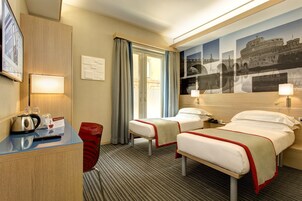 A hotel room with two beds, a desk with a kettle, a chair, and a large wall mural.
