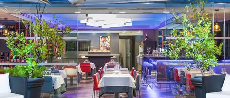 An indoor restaurant with tables and chairs, a bar area, and potted plants.