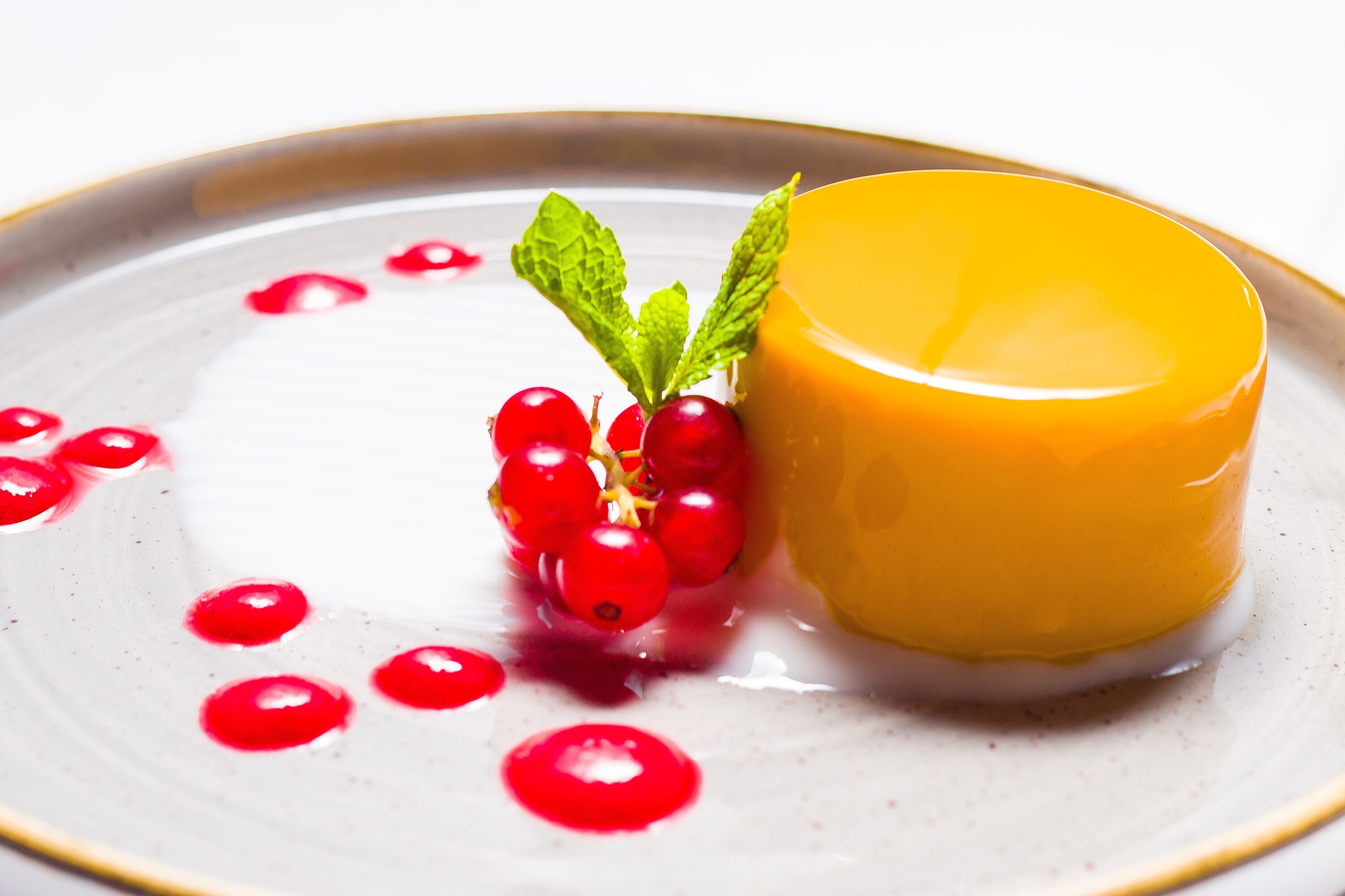 A dessert with a yellow dome, red berries, and mint leaves on a plate.