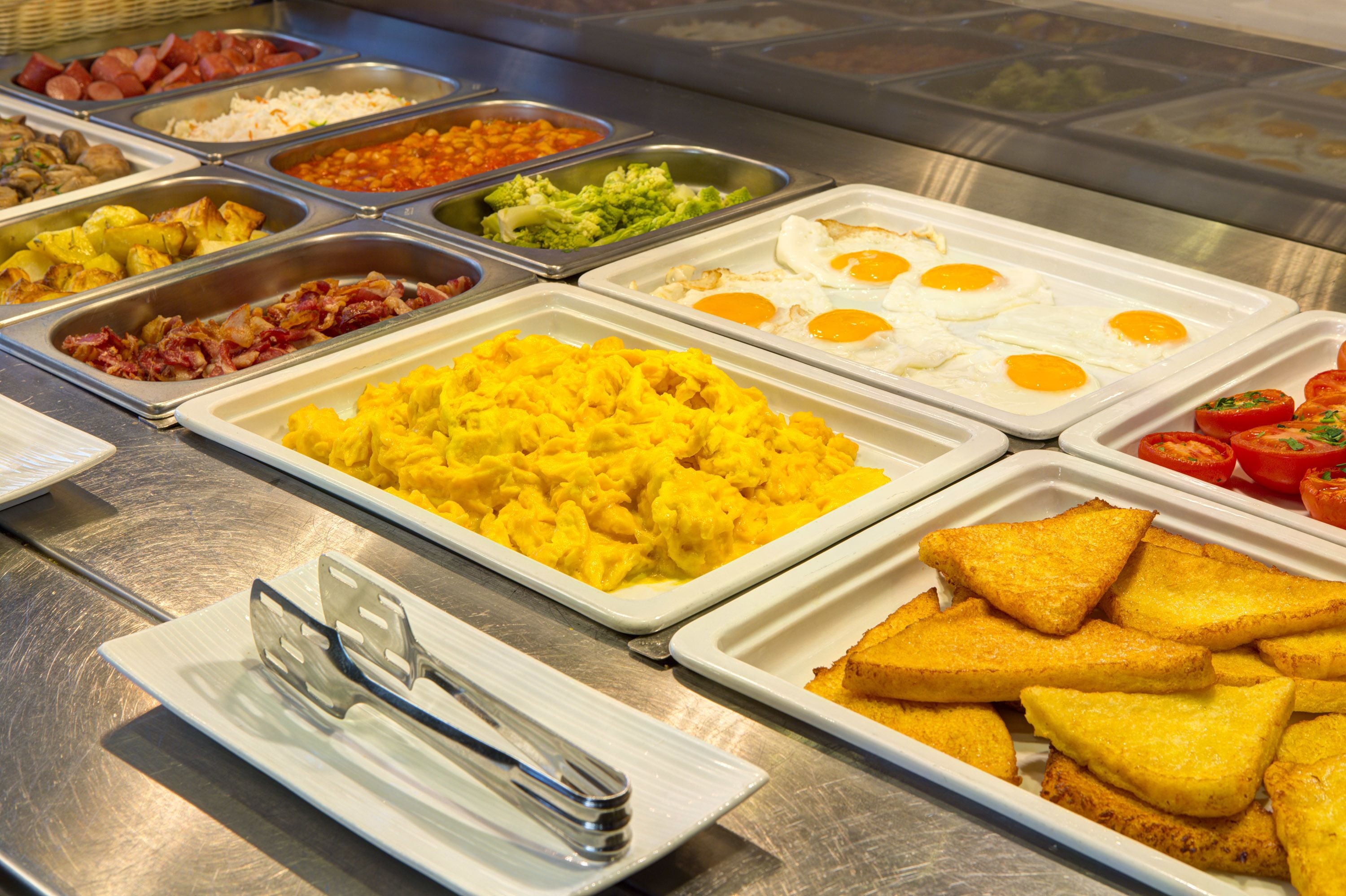 A buffet with various food options including scrambled eggs, bacon, potatoes, and toast.