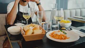 A dining table with a plate of pasta, a bowl of bread, and glasses of white wine.