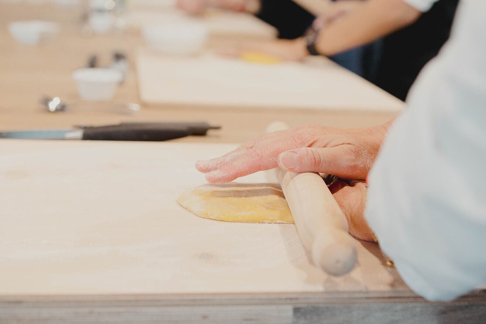 A person rolling dough on a wooden surface with a rolling pin.