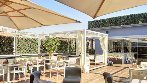 An outdoor patio with wooden flooring, white and black chairs, and large umbrellas. - iQ Hotel Roma (Rome)