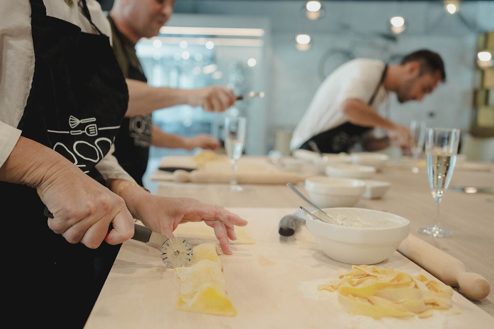 A kitchen scene with chefs preparing food, a rolling pin, a bowl, and a wine glass on the counter.