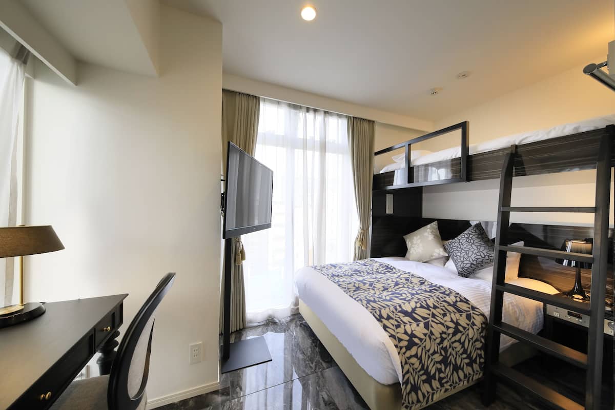 Une chambre d’hôtel équipée d’un lit, d’un bureau, d’une chaise, d’une télévision et d’un lit superposé.