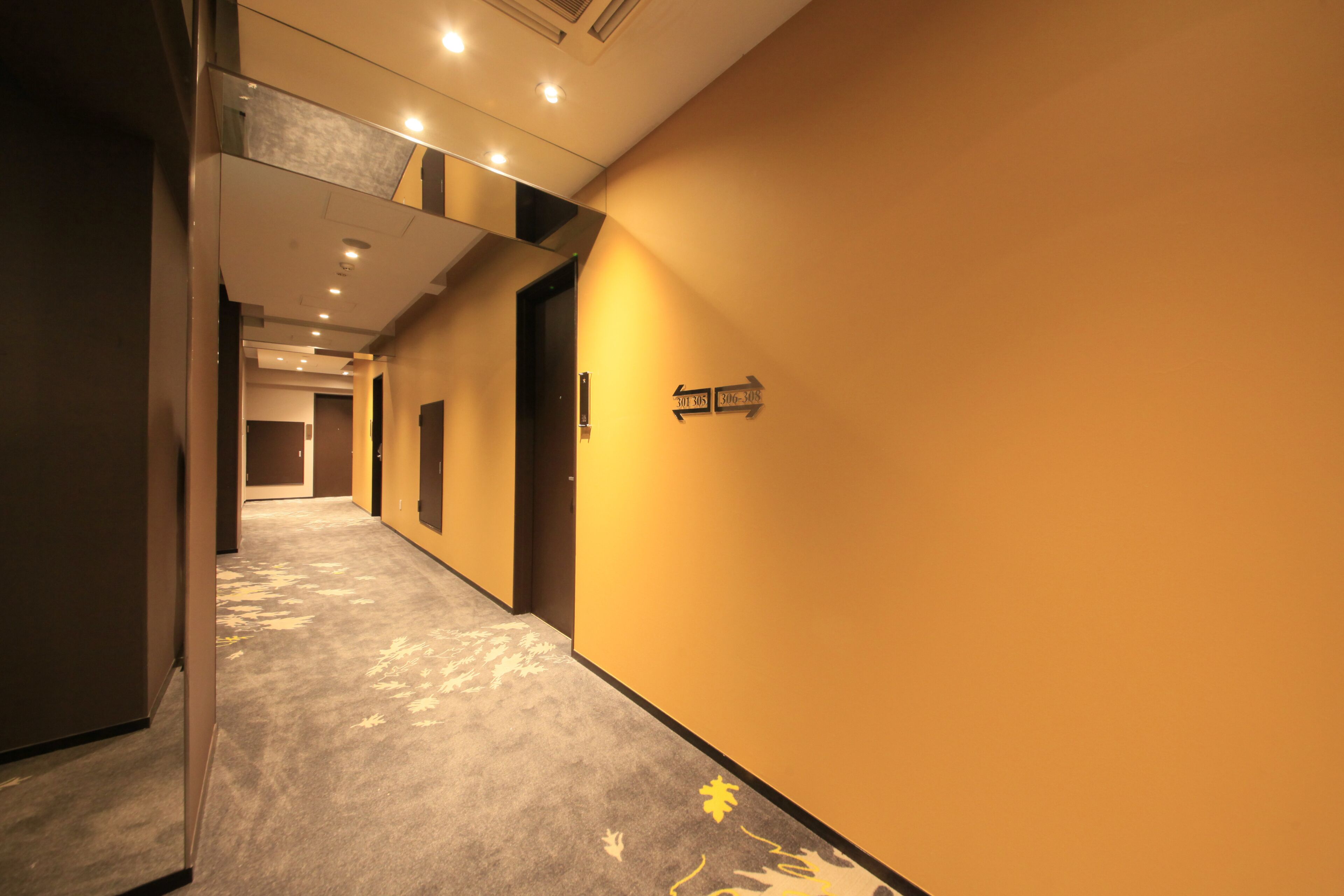 Un couloir d’hôtel avec des panneaux de signalisation, un revêtement de sol en moquette et un design de plafond moderne.