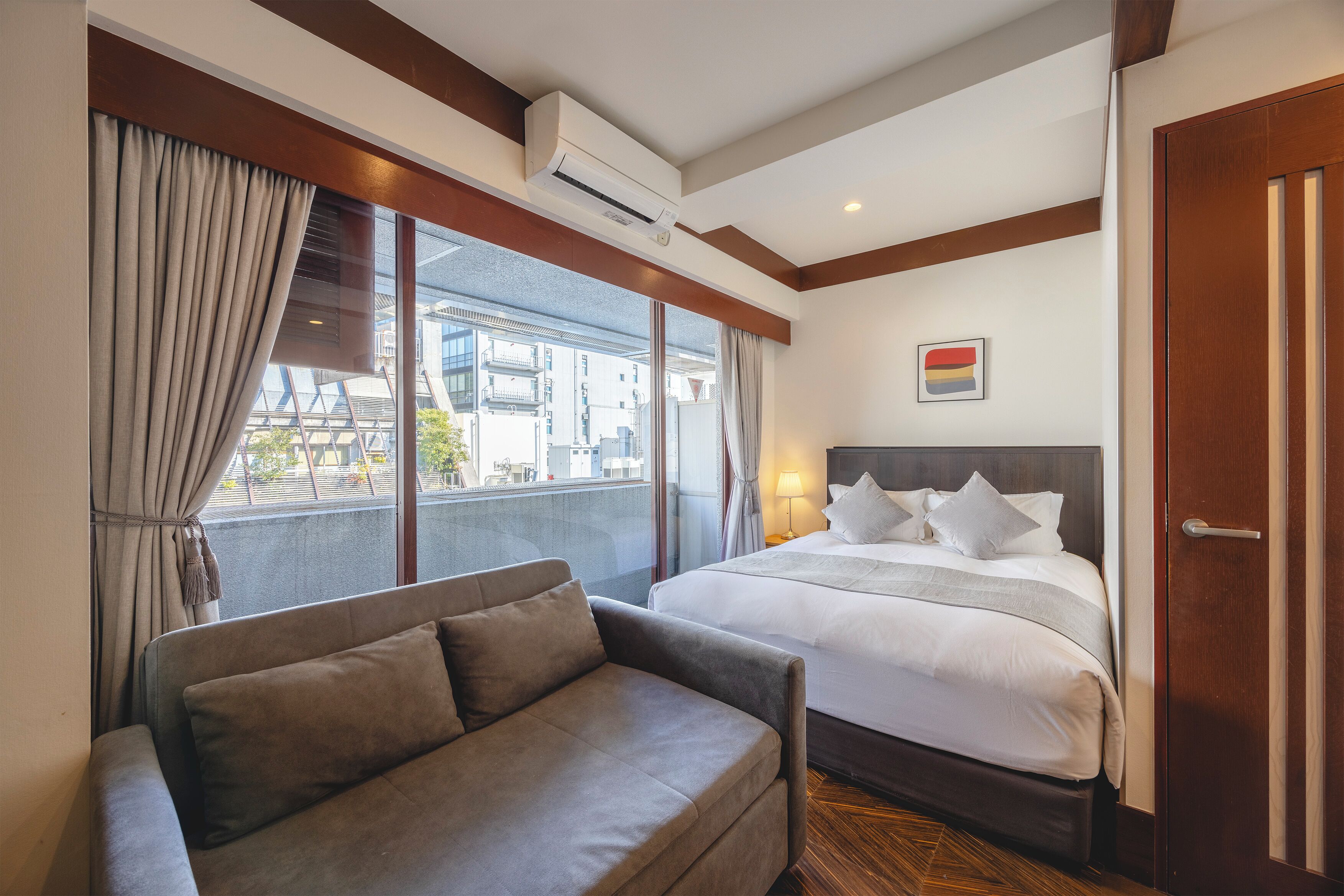 Habitación de hotel con cama, sofá, ventana con cortinas, aire acondicionado y puerta.