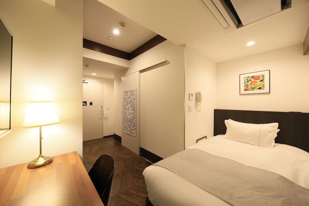 Une chambre d’hôtel comprenant un lit, un bureau avec une lampe, un téléphone fixé au mur et une porte donnant accès à une salle de bain.