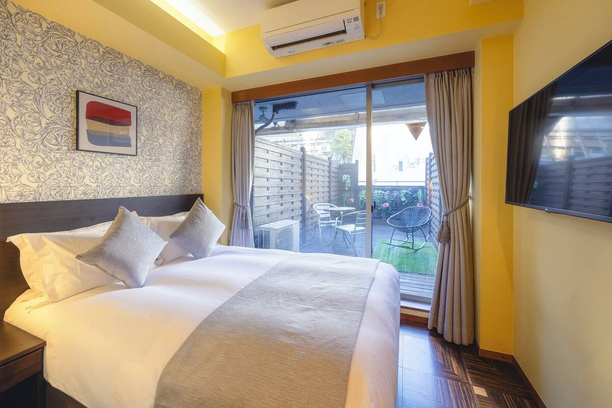 Une chambre d’hôtel avec un grand lit, une télévision, une fenêtre avec des rideaux et un mur décoré de motifs.