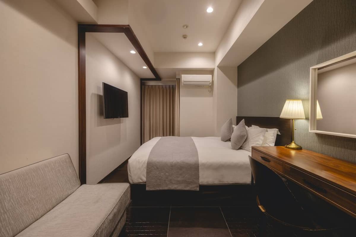 Une chambre d’hôtel avec un lit, une télévision, un bureau avec une lampe et une fenêtre avec des rideaux.