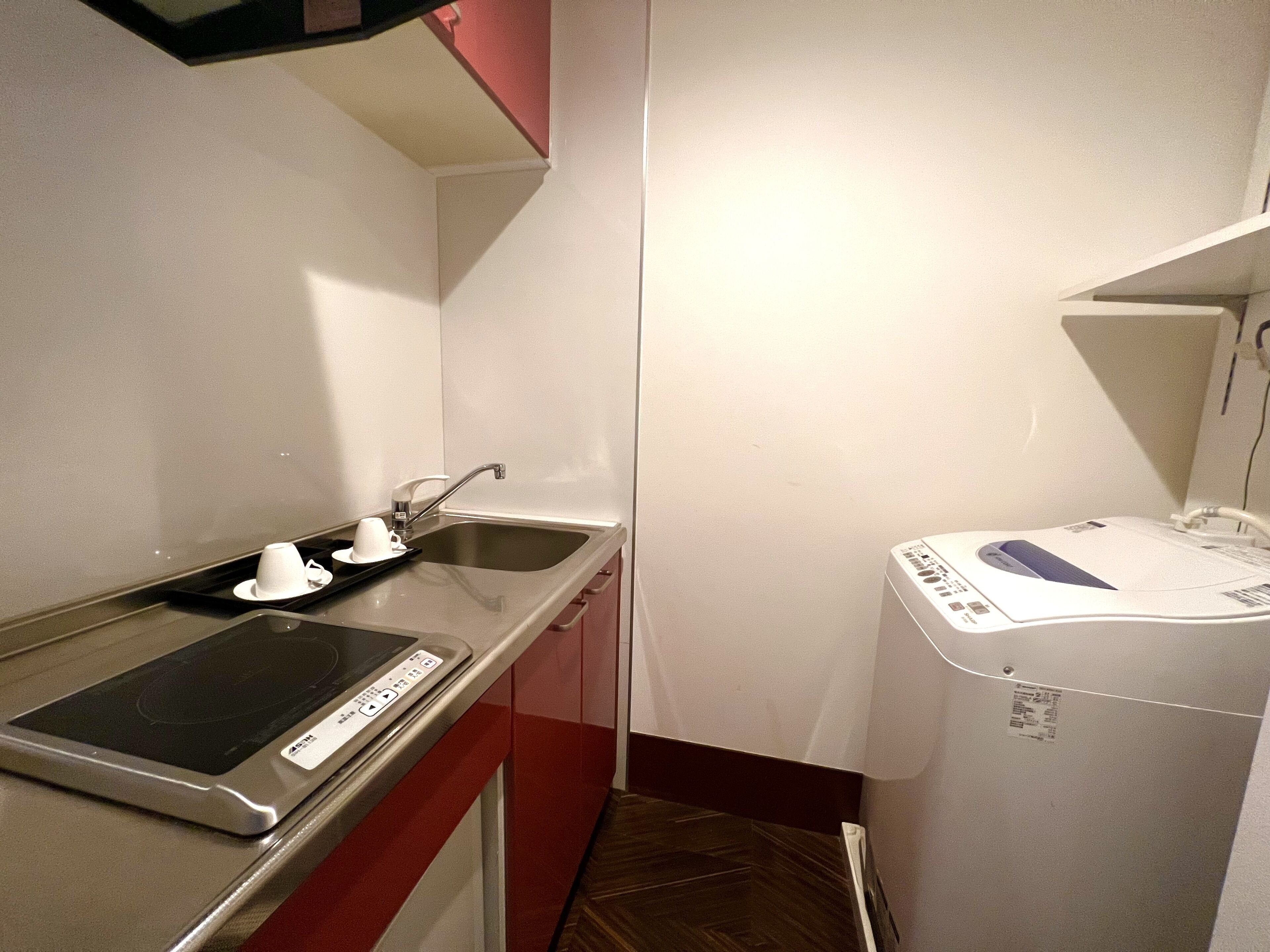 Ett litet, praktiskt kök med en inbyggd spis, en diskho och en kompakt tvättmaskin.