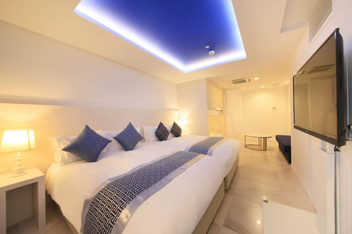 Une chambre d’hôtel moderne dotée d’un grand lit, de tables de chevet, d’un téléviseur à écran plat et d’un luminaire au plafond.