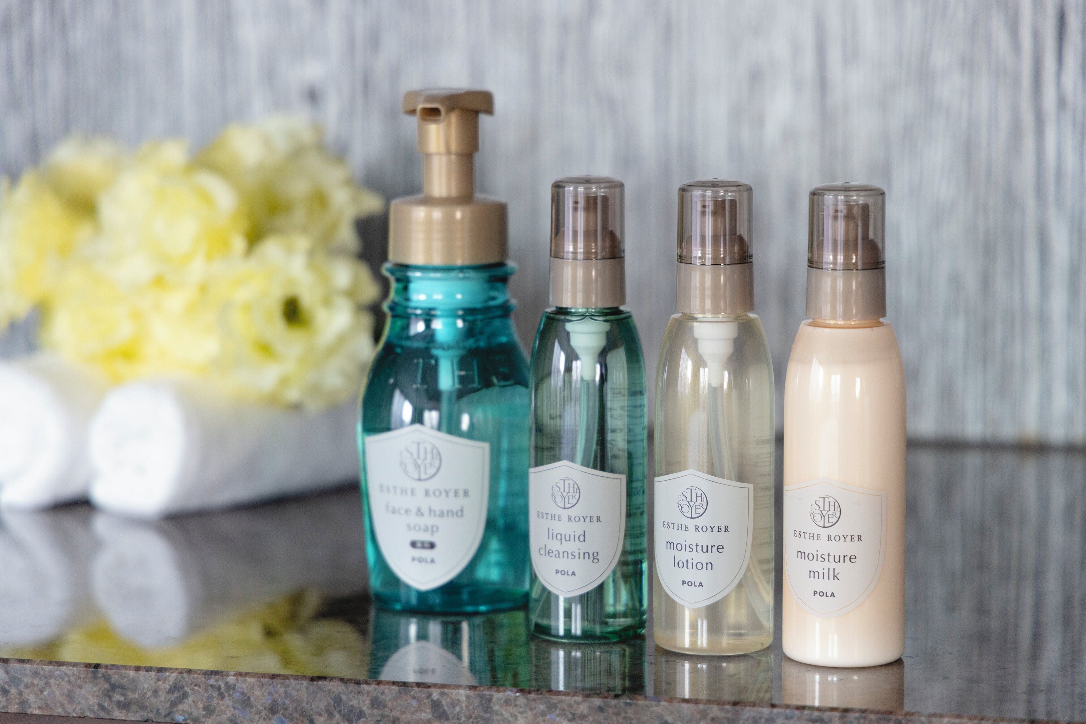 Four bottles of ESTHE ROYER skincare products on a reflective surface.