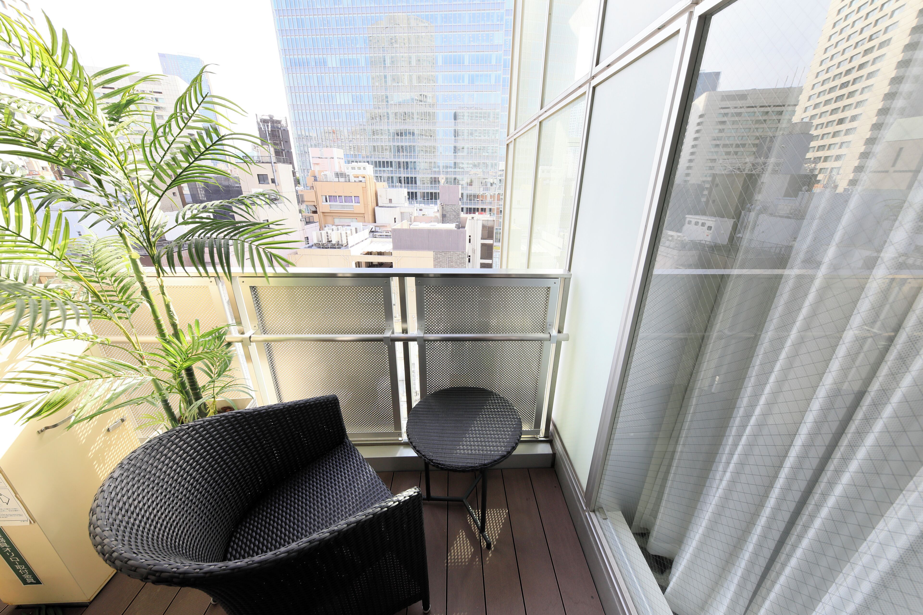 A balcony with a wicker chair, a small table, and a potted plant.