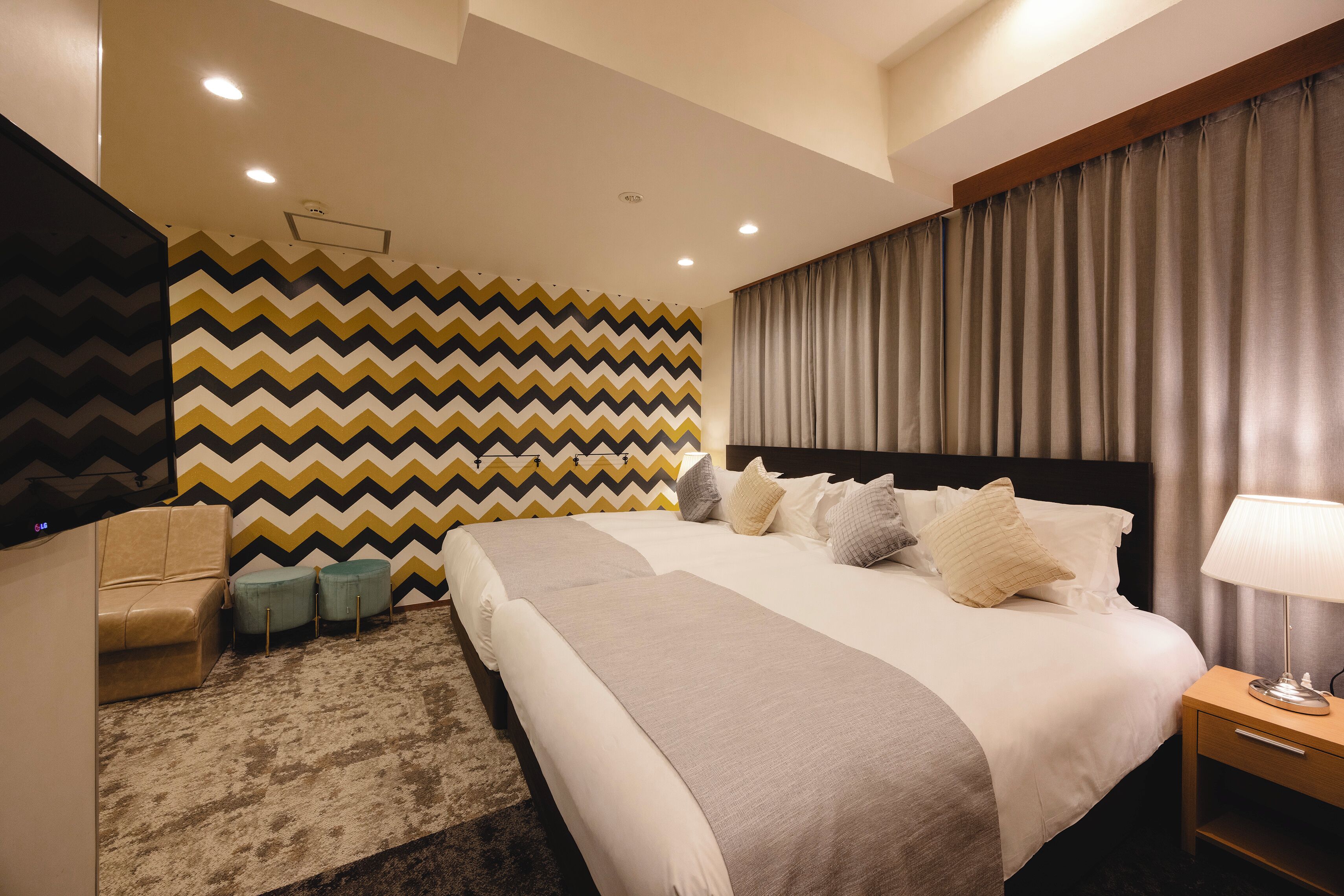 Une chambre d’hôtel moderne avec un grand lit, un bureau, une chaise et un mur décoré d’un motif.