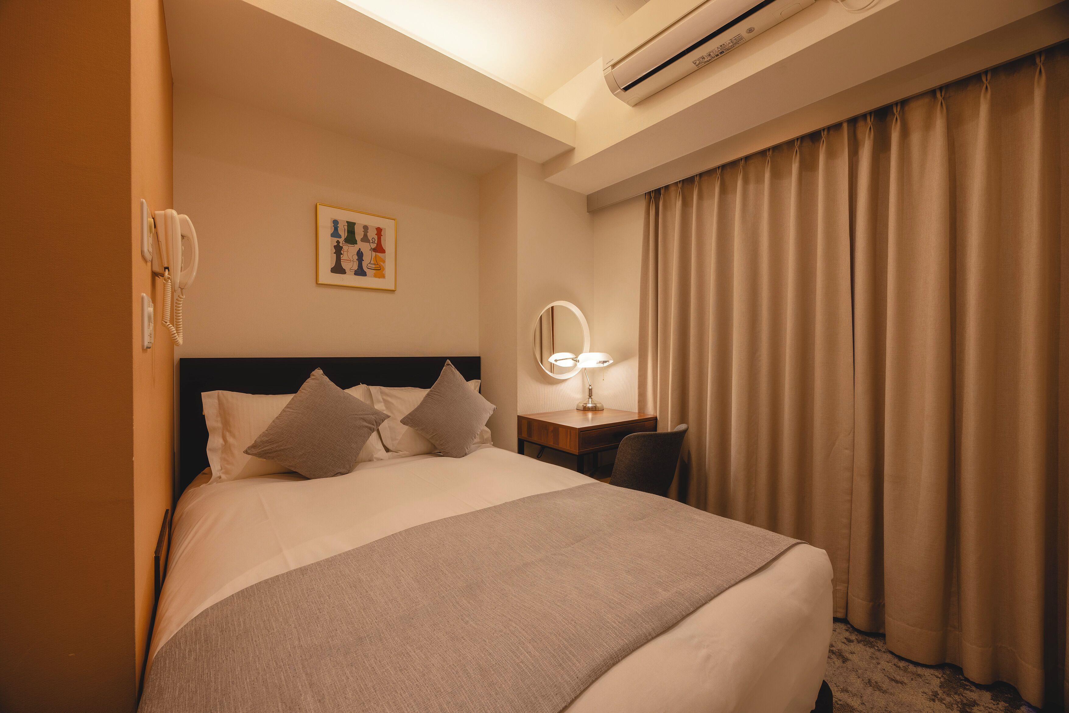 Habitación de hotel con cama, escritorio con lámpara, teléfono y espejo montado en la pared.
