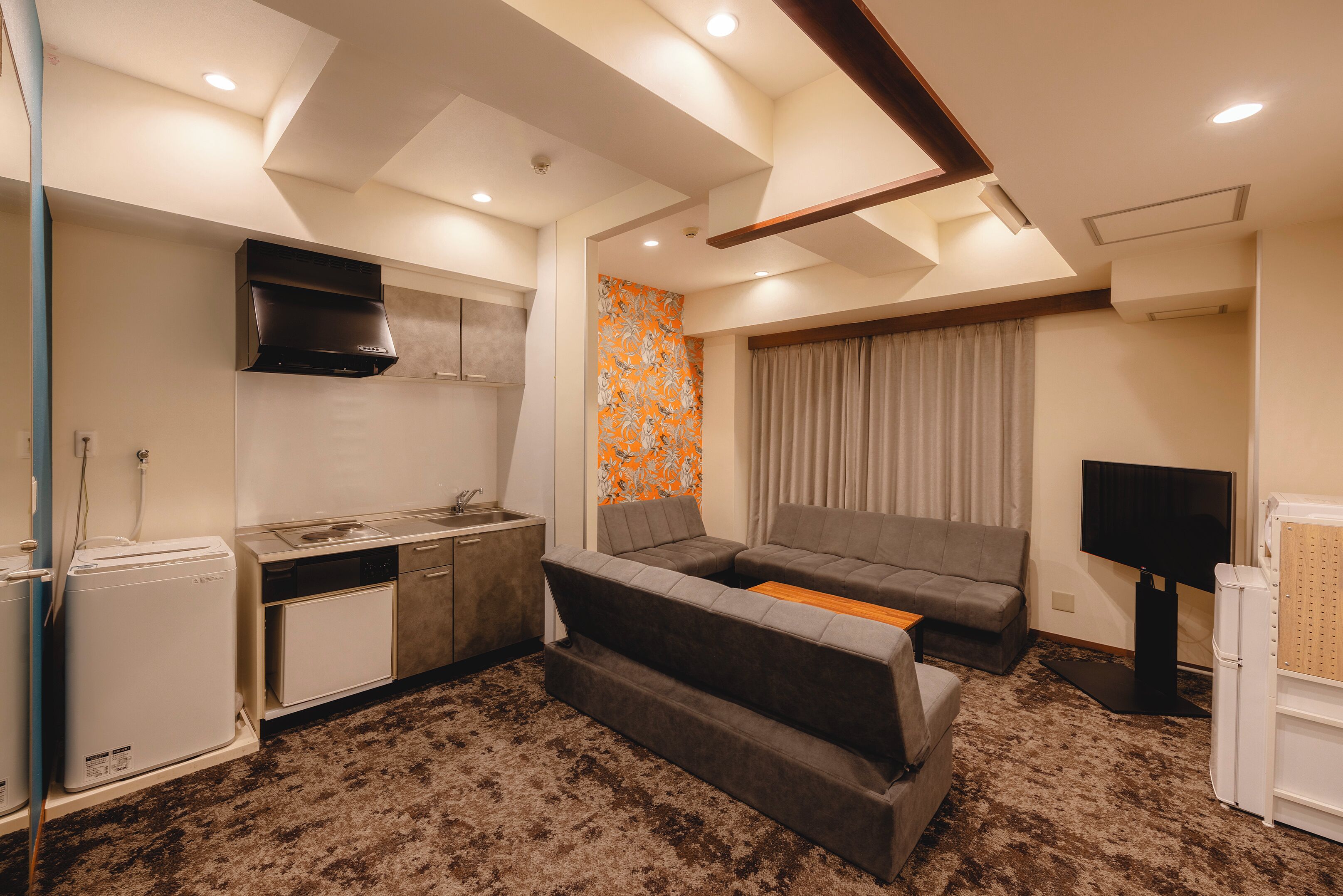 A compact living space with a kitchenette, sofa, and a flat-screen TV.