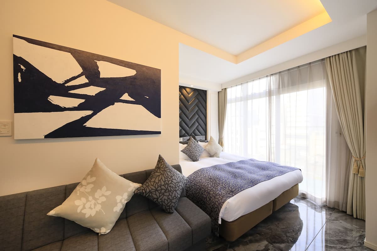 Une chambre moderne avec un grand lit, un canapé agrémenté de coussins à motifs, un grand tableau abstrait et une tête de lit à motifs en chevrons.
