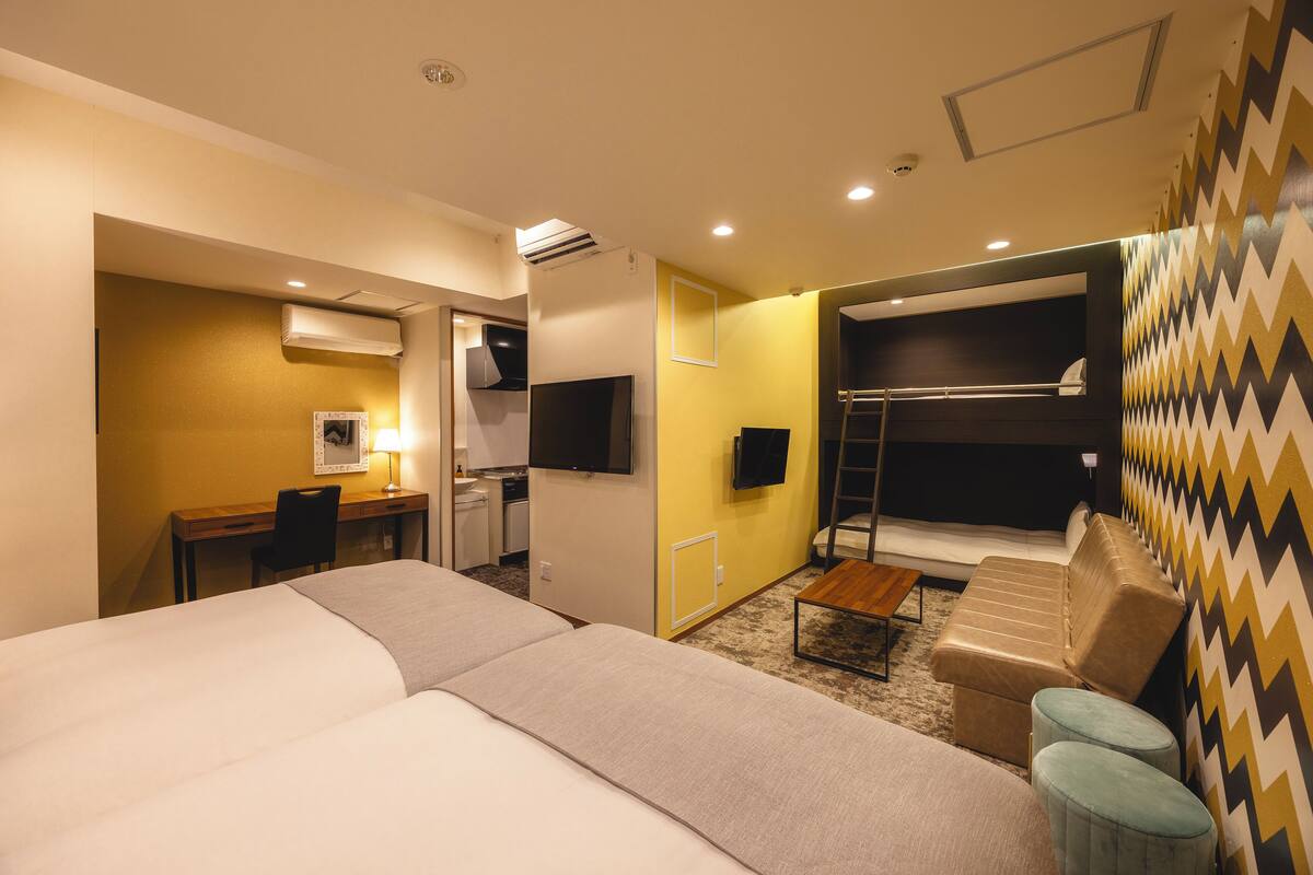 Une chambre d’hôtel avec un lit, un bureau, une chaise, une télévision, un lit superposé et un mur décoré de motifs.