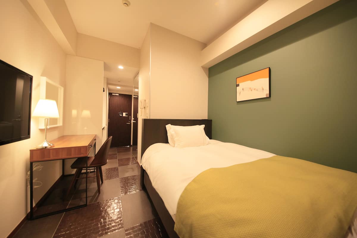 Une chambre d’hôtel avec un lit, un bureau, une chaise, une lampe et un tableau au mur.