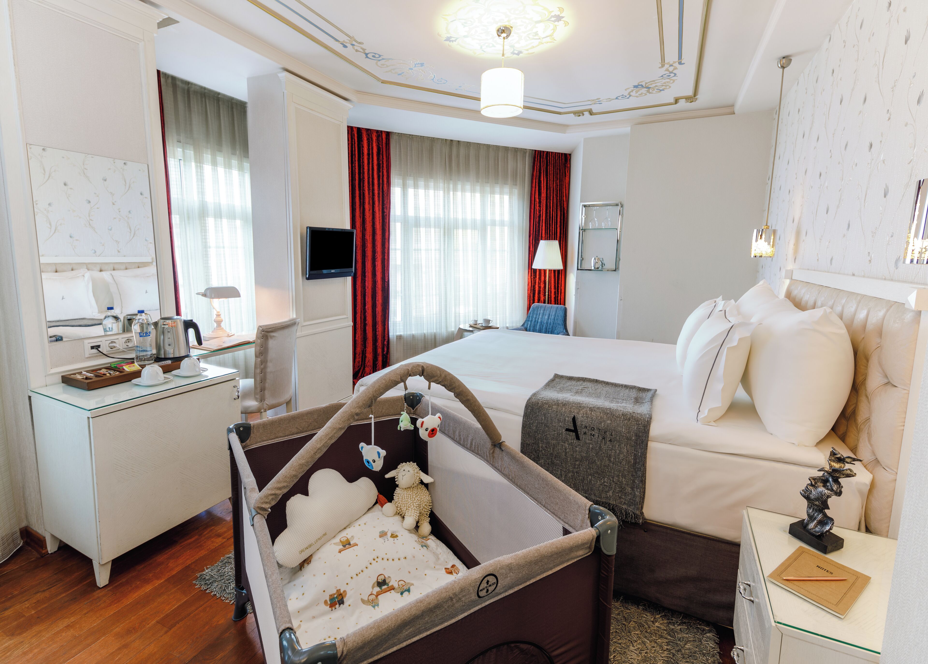 Une chambre d’hôtel comprenant un lit, un bureau avec un téléviseur à écran plat, un minibar et une grande fenêtre avec des rideaux.