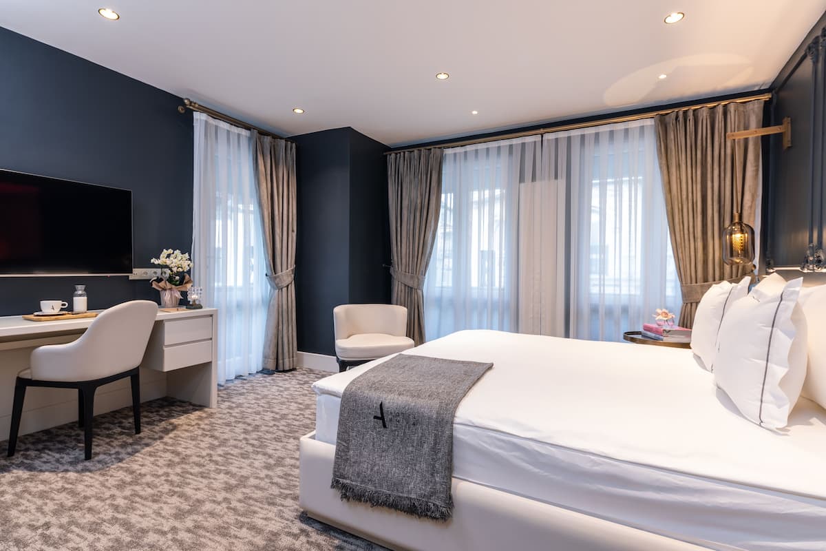 Une chambre d’hôtel moderne dotée d’un grand lit, d’un bureau avec une chaise, d’une télévision et d’une fenêtre avec des rideaux.