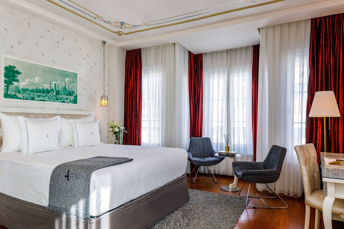 Une chambre d’hôtel avec un grand lit, deux chaises, une petite table et une lampe.