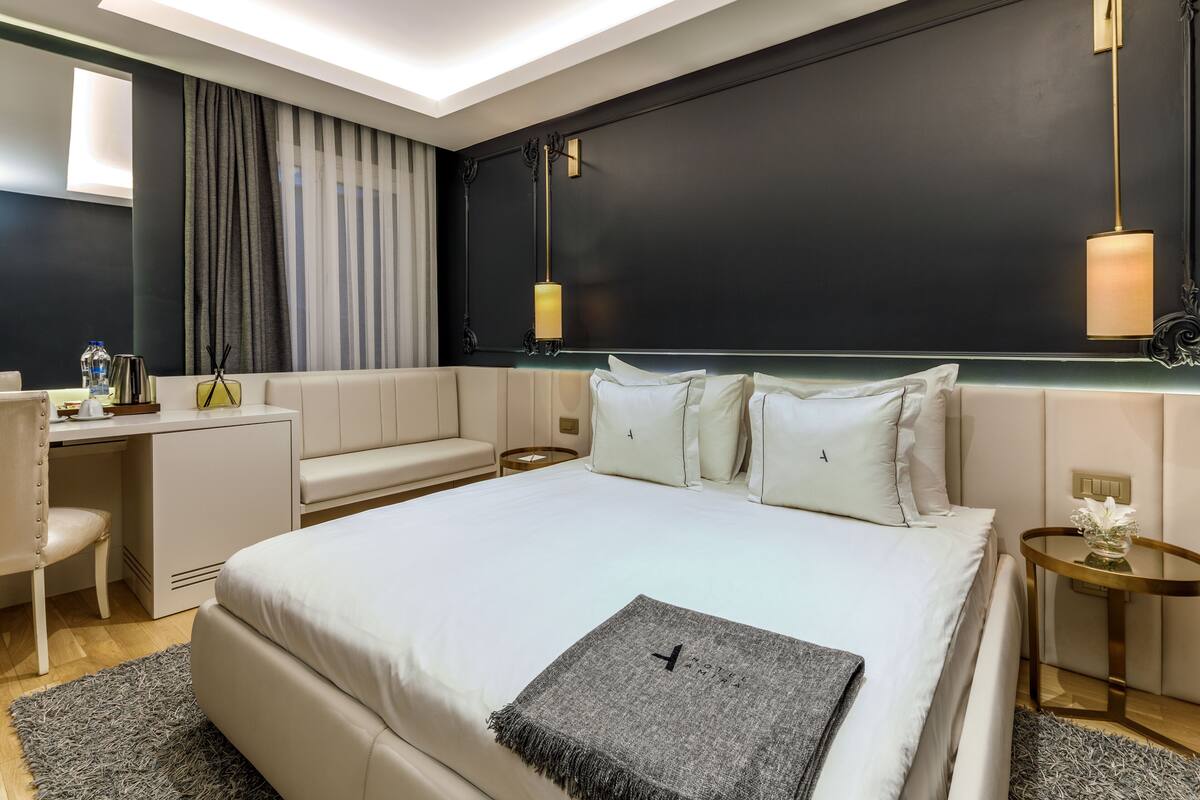 Une chambre d’hôtel moderne, dotée d’un grand lit, d’un bureau, d’une chaise et d’une petite table sur laquelle est posé un vase de fleurs.
