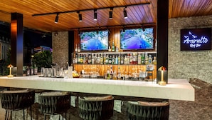 A bar area with a long counter, multiple stools, and two televisions displaying a beach scene. - Hotel Amira Istanbul (Istanbul)