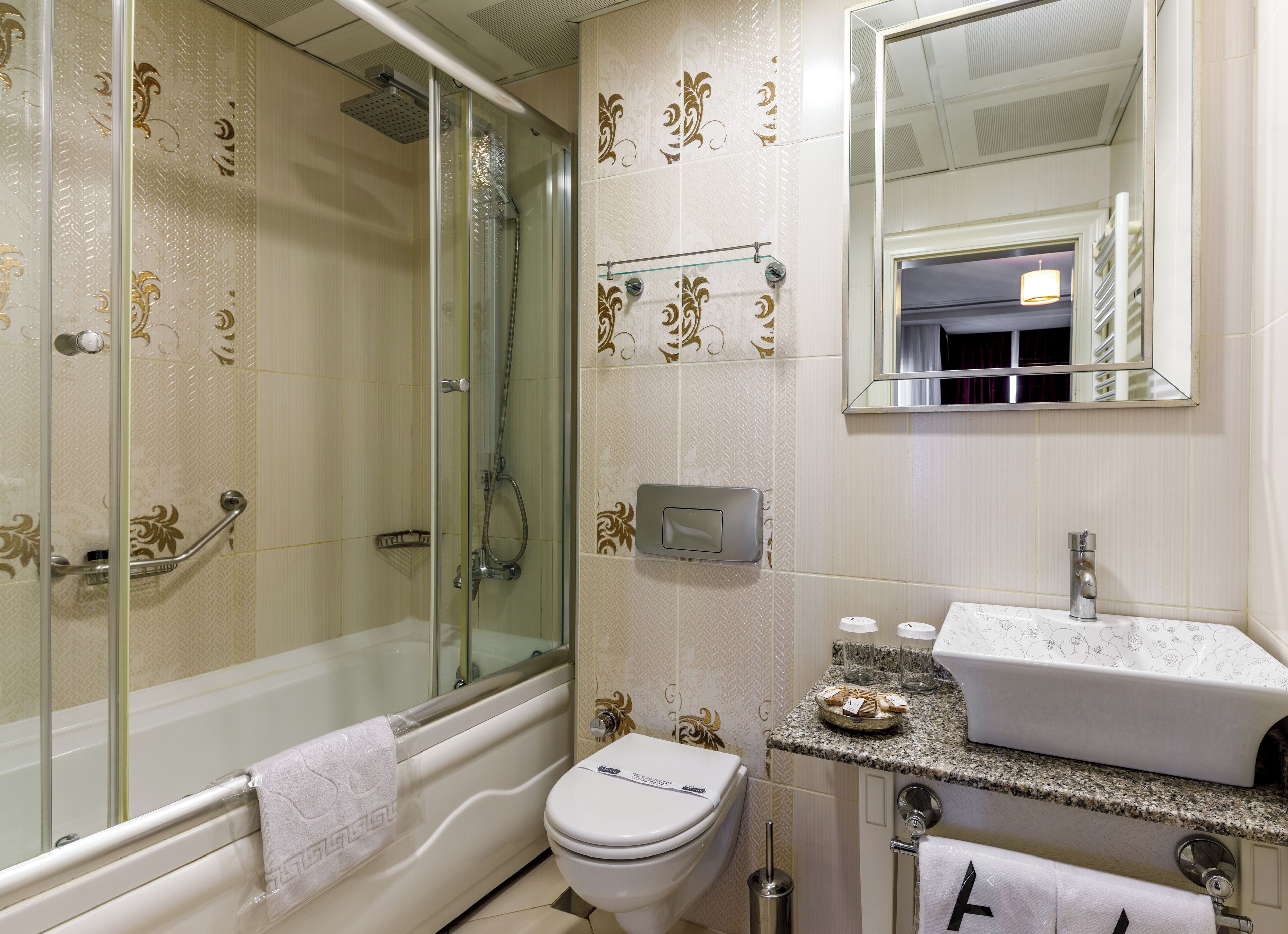 A bathroom with a glass-enclosed shower, a white toilet, a sink with a marble countertop, and a mirror above the sink.