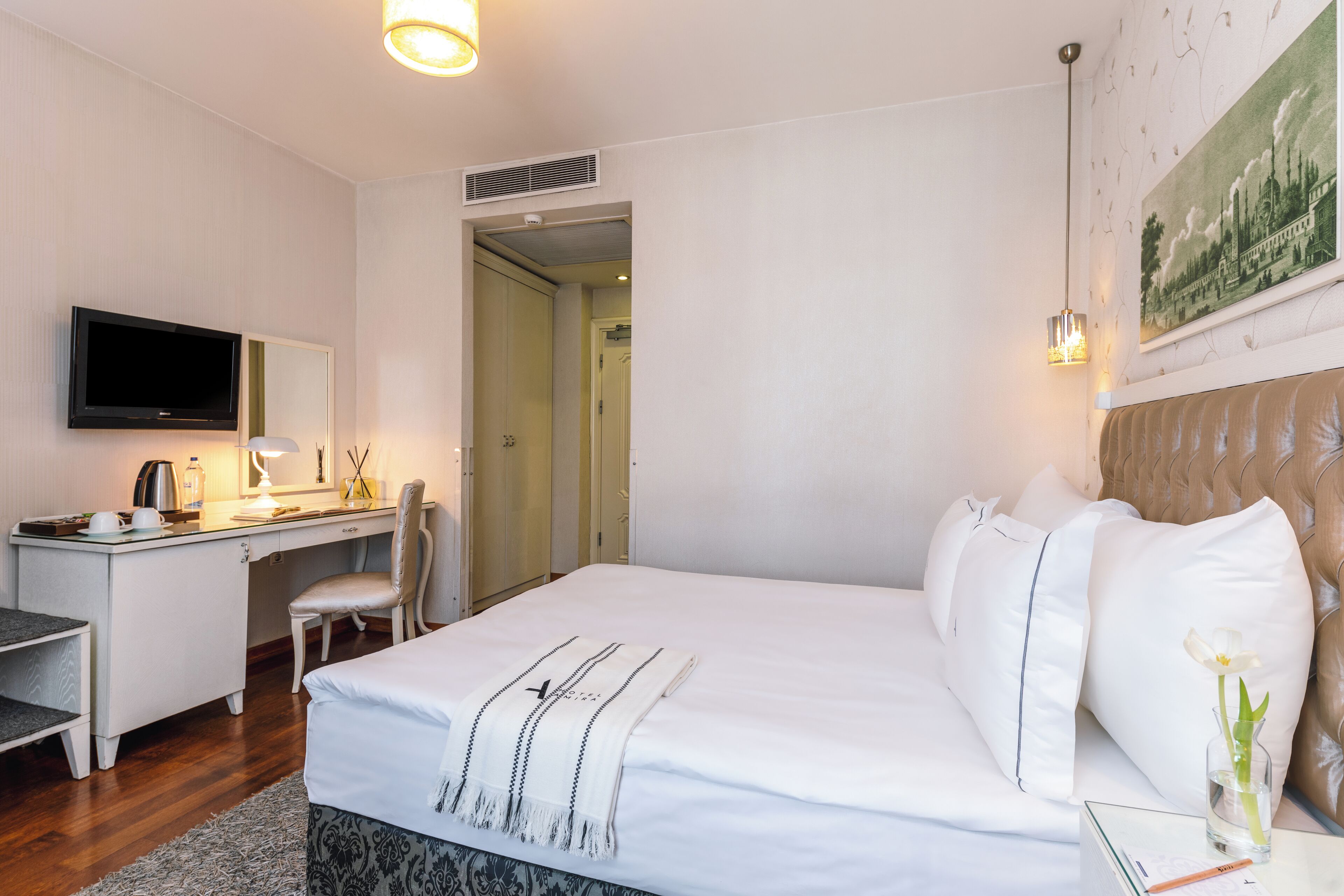 A hotel room with a bed, desk, chair, TV, and a painting on the wall.