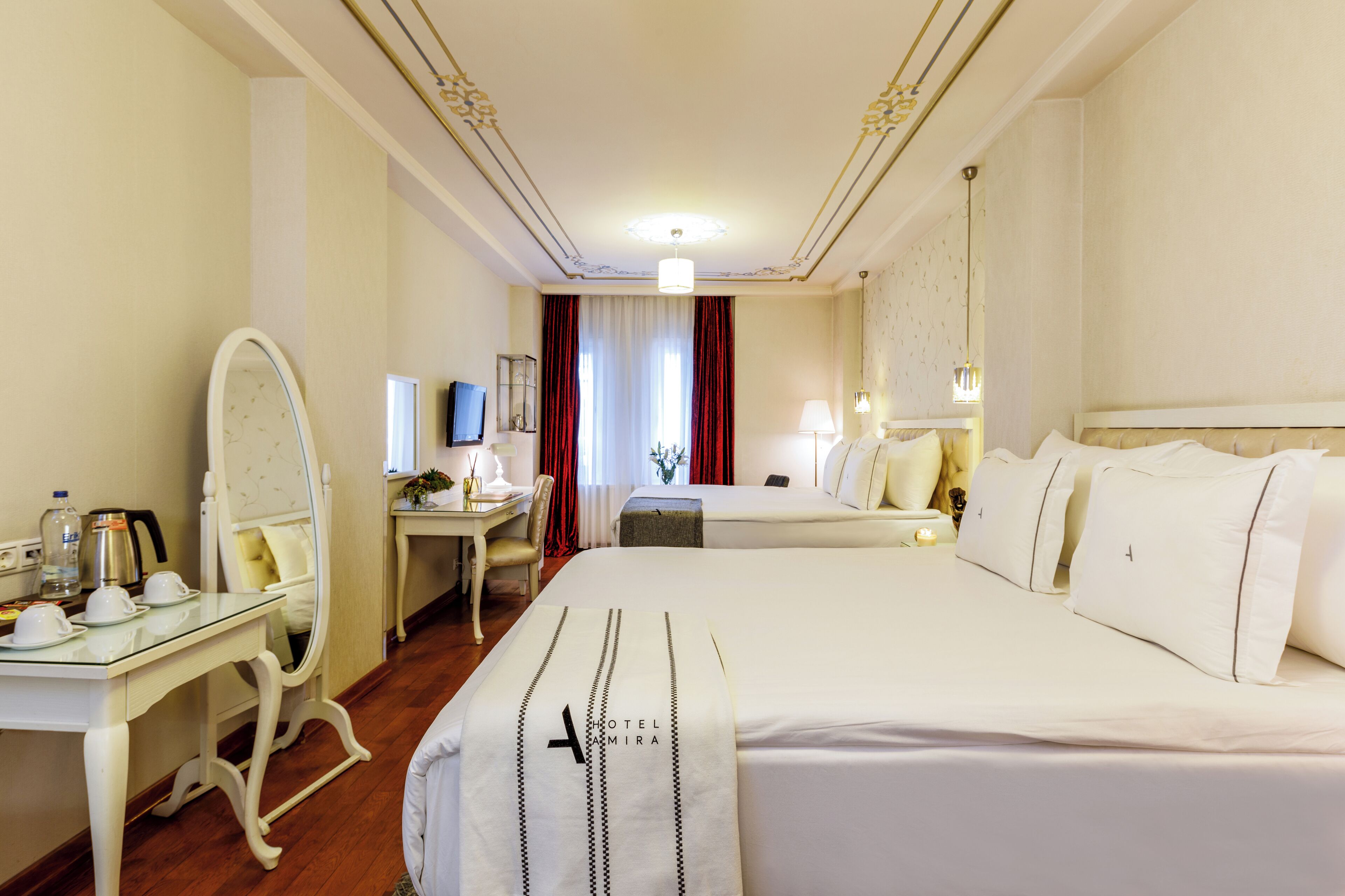 Habitación de hotel con una cama grande, un escritorio con silla, un espejo, un televisor y una ventana con cortinas.