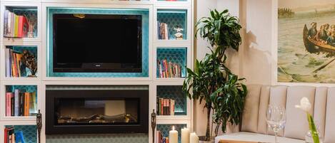 A living room with a fireplace, bookshelves, a television, and a dining area with a table set for two.