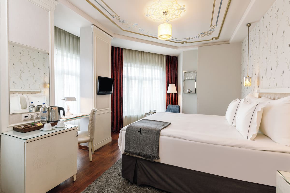 Une chambre d’hôtel avec un grand lit, un bureau doté d’un téléviseur à écran plat, une chaise, une petite table et un miroir.