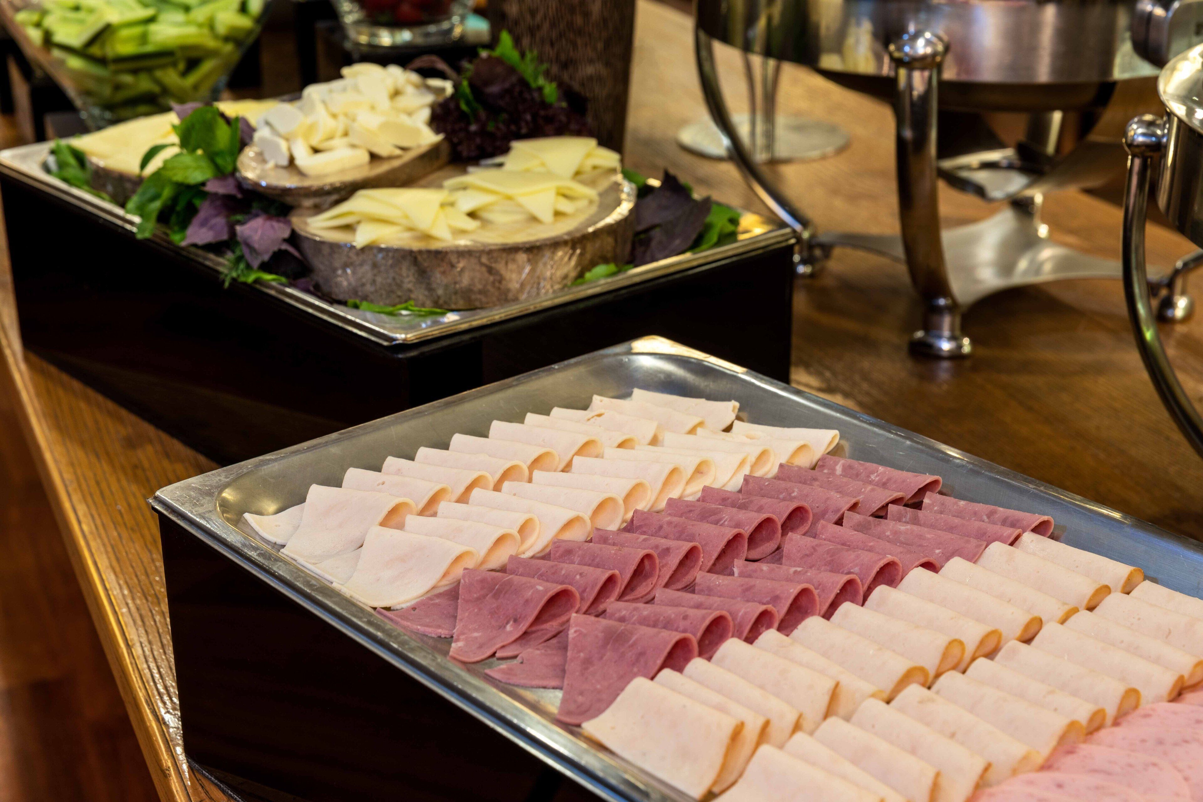 A buffet with neatly arranged trays of sliced meats and cheeses.