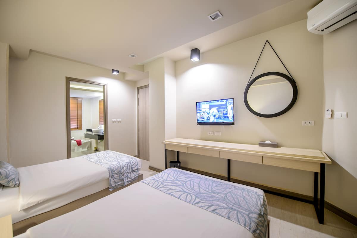 Une chambre d’hôtel avec deux lits, un bureau, une télévision et un miroir.