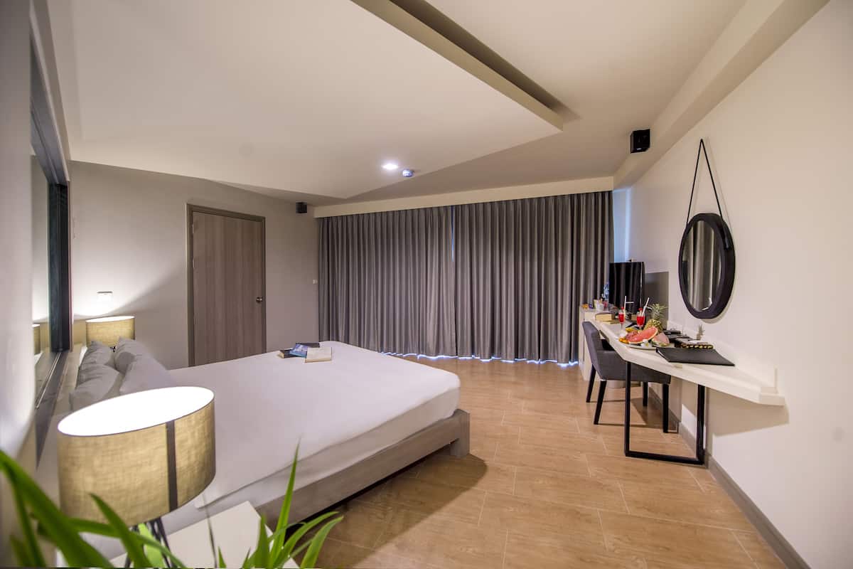 Une chambre d’hôtel moderne dotée d’un grand lit, d’un bureau avec un ordinateur portable, d’un miroir et offrant une vue sur la ville.