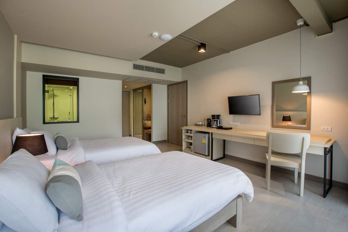 Une chambre d’hôtel avec deux lits, un bureau, une chaise, une télévision et un miroir.