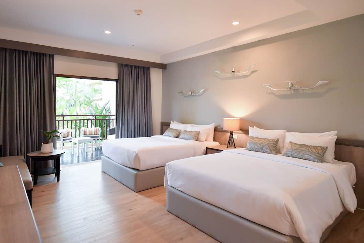 Une chambre d’hôtel avec deux lits, un bureau, une chaise, un balcon avec des rideaux et une vue sur la verdure.