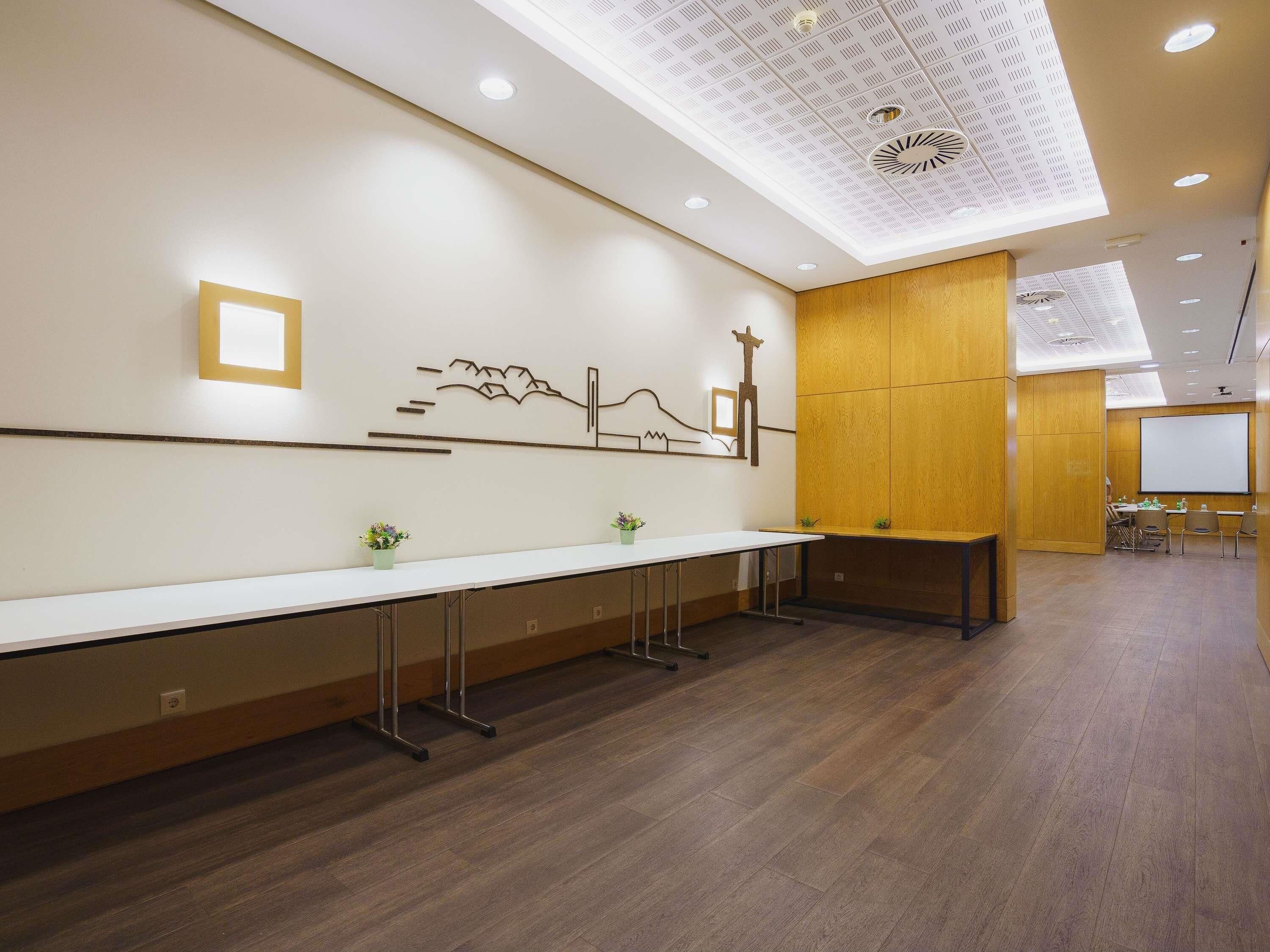A conference room with a long table, chairs, a projector screen, and a wooden accent wall.