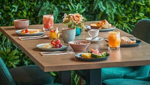 A breakfast setting with a variety of food items and drinks on a table, surrounded by lush greenery. - Mercure Lisboa Almada (Almada)