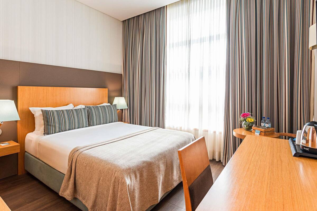 A hotel room with a bed, a wooden headboard, a nightstand, a table, and a chair.