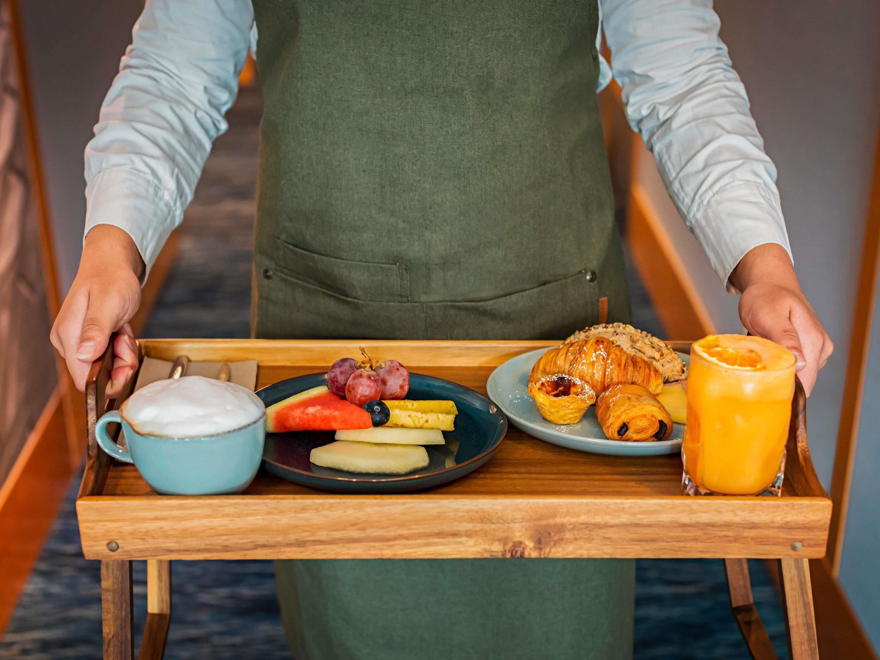 Un plateau contenant des éléments pour le petit-déjeuner, notamment un croissant, des fruits, une boisson et une tasse de café.