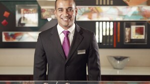 A man in a suit standing in a lobby with a modern design, including abstract art on the walls and a clear glass display case in the foreground. - Mercure Lisboa Almada (Almada)