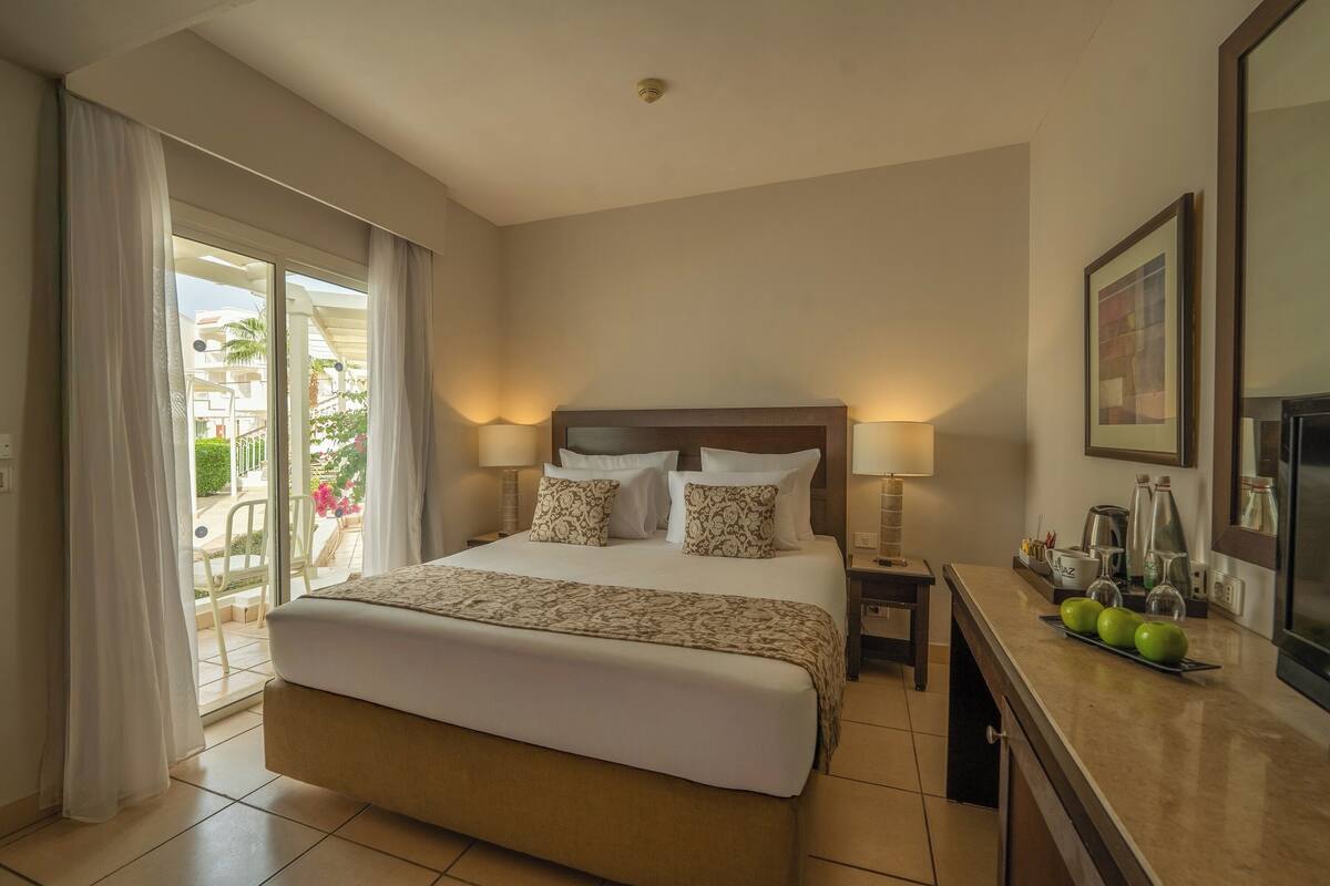 Une chambre d’hôtel avec un grand lit, deux tables de chevet avec des lampes, une commode et une vue sur le balcon extérieur.