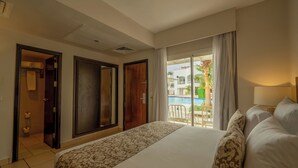 Une chambre d’hôtel avec un grand lit, une salle de bain avec des toilettes et un lavabo, et un balcon avec vue sur la piscine.
