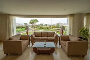 Ein Wohnzimmer mit einer Sofagarnitur, einem Couchtisch und Blick auf eine angelegte Grünanlage mit Palmen und Bergen.