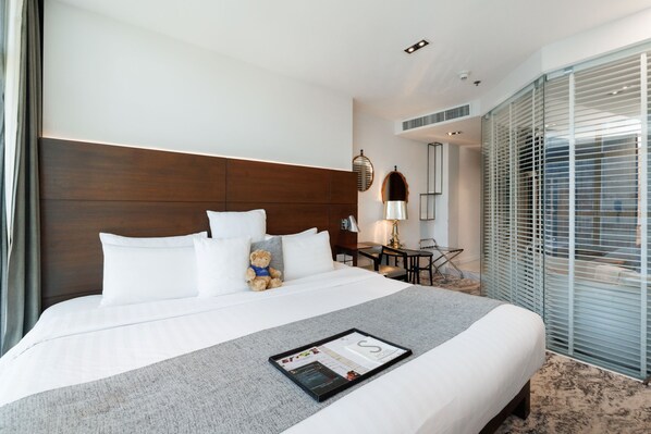 A hotel room with a large bed, a bedside table, a lamp, and a window with blinds.