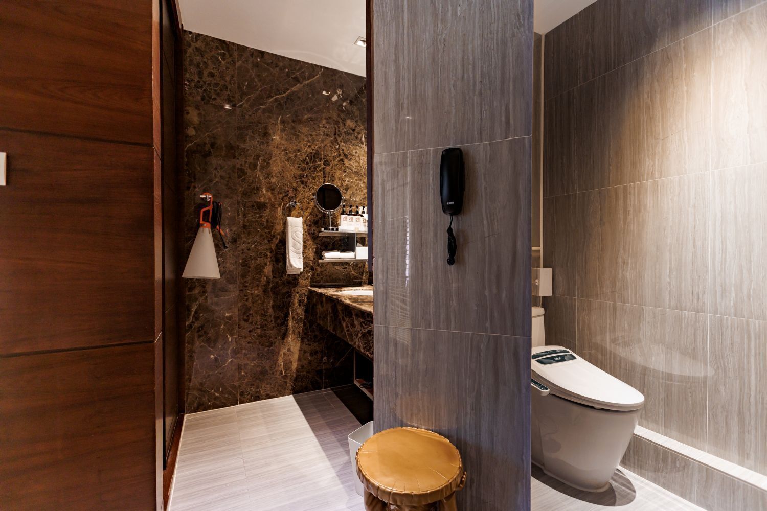 Et moderne badeværelse med en marmorvæg, toilet, vask, spejl og et håndklædestativ.
